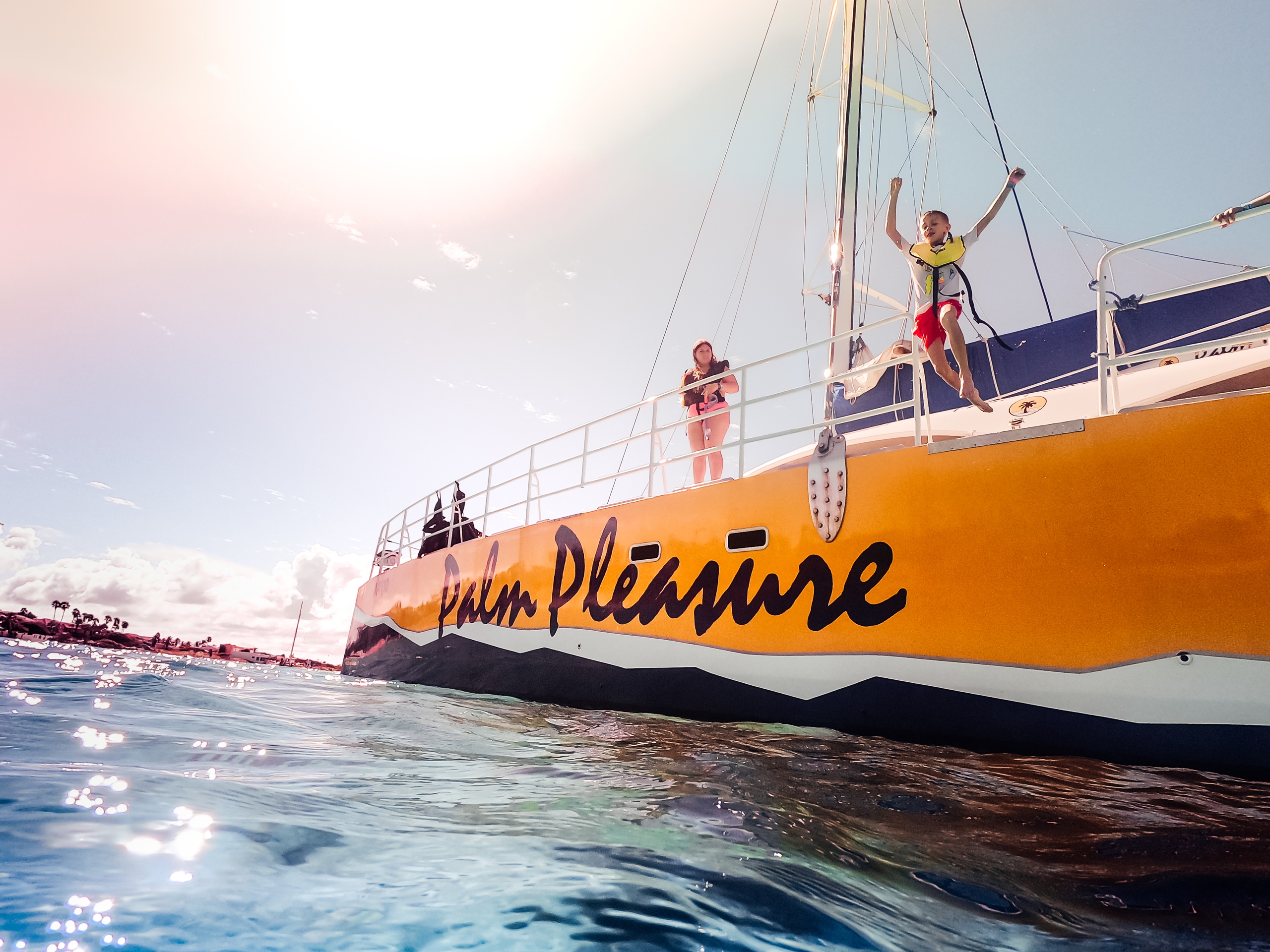 People on a yellow boat named 'Palm Pleasure' in sunny ocean waters.
